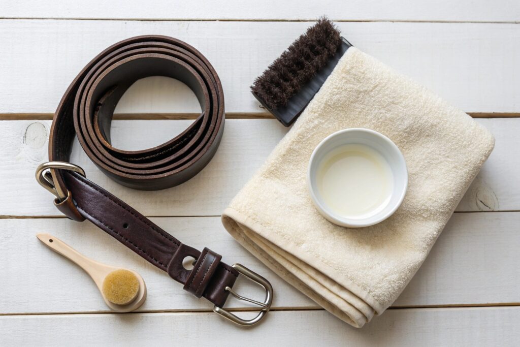 Flat lay of a sealed brown leather belt with a silver buckle, alongside a soft towel, leather care brush, and conditioning oil—ideal for promoting Chinese leather belt manufacturers focused on quality and maintenance.