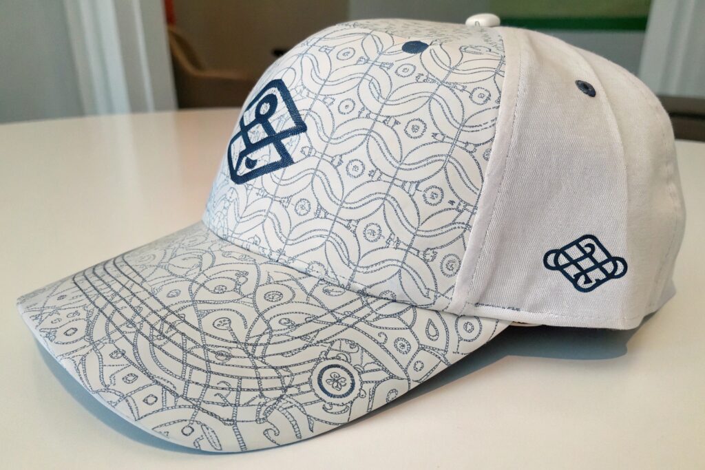 A white baseball cap with a blue geometric pattern and logos on a white table