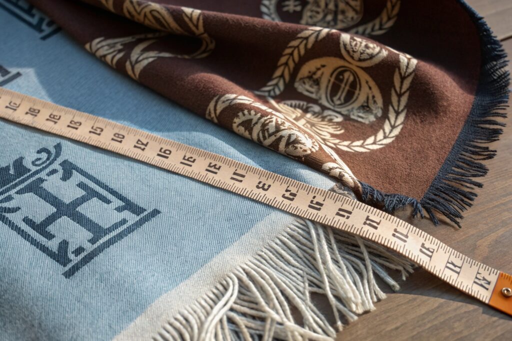 Detailed close-up showing luxury scarf edges with hand-rolled hems and fringe, featuring a measuring tape to highlight precise sizing and craftsmanship