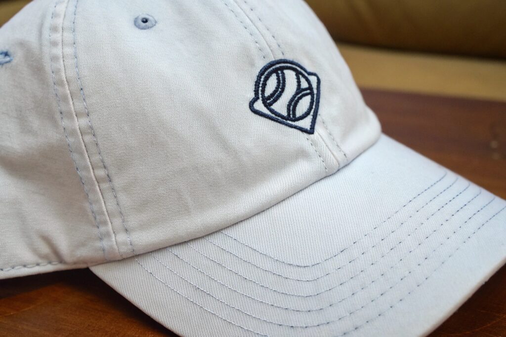 Three baseball caps in navy blue, denim blue, and light gray, each with a small embroidered logo