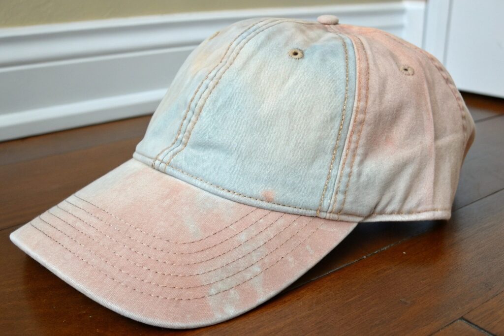 A light gray baseball cap with a dark blue embroidered design of a tennis ball