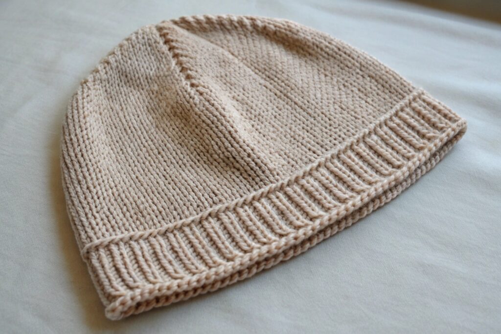 A beige knitted beanie hat on a light gray surface