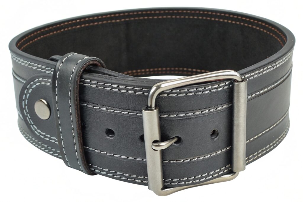A dark brown leather belt with white stitching and a silver buckle on a workbench with leatherworking tools